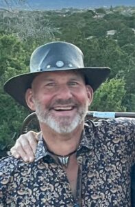 Man with grey beard and black hat, smiling